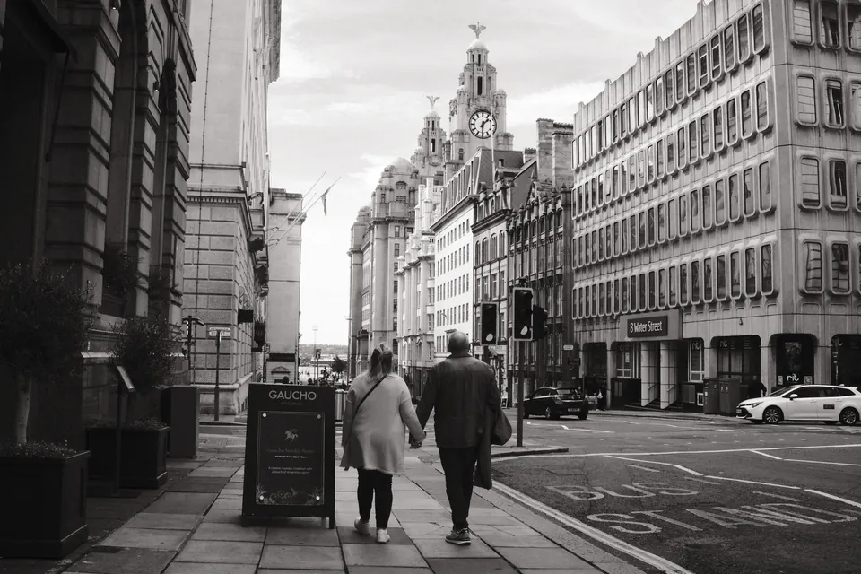 Two pedestrians walk down Water Street towards the Royal Liver Building.